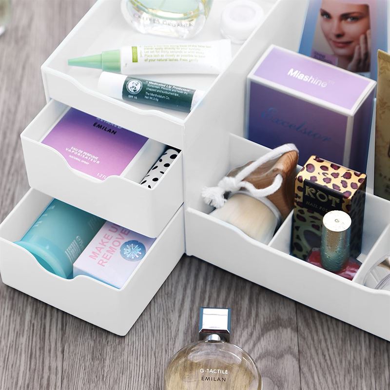 The UNIQ Organiser for makeup & skincare products with 9 compartments in White by UNIQ neatly holds boxed soap, a makeup remover tube, a face brush, cotton swabs, and assorted cosmetics on a wooden surface.