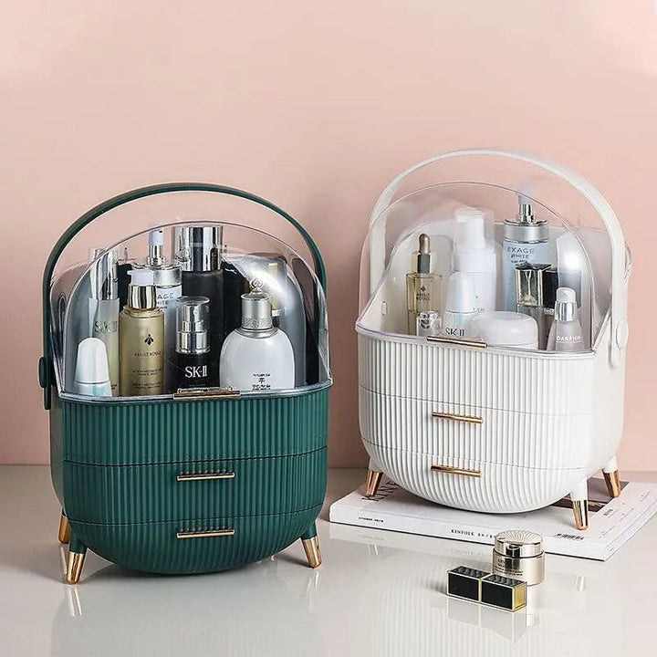 Two chic UNIQ Retro Makeup Box Organisers by UNIQ in Dark Mint and Dark Green feature oval shapes, handles, gold legs, and clear covers to store skincare or cosmetics. Nearby, a few small containers rest on a white surface.