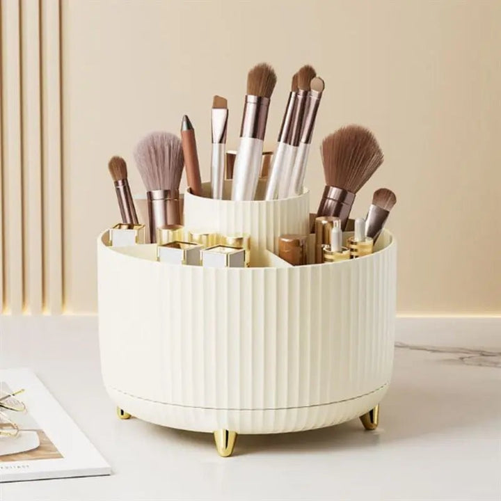 The UNIQ Rotating Makeup Organiser in cream white, by UNIQ, features gold legs and a round design to neatly hold brushes, lipsticks, and pencils. Stylishly displayed on a marble surface in a neutral-toned room.